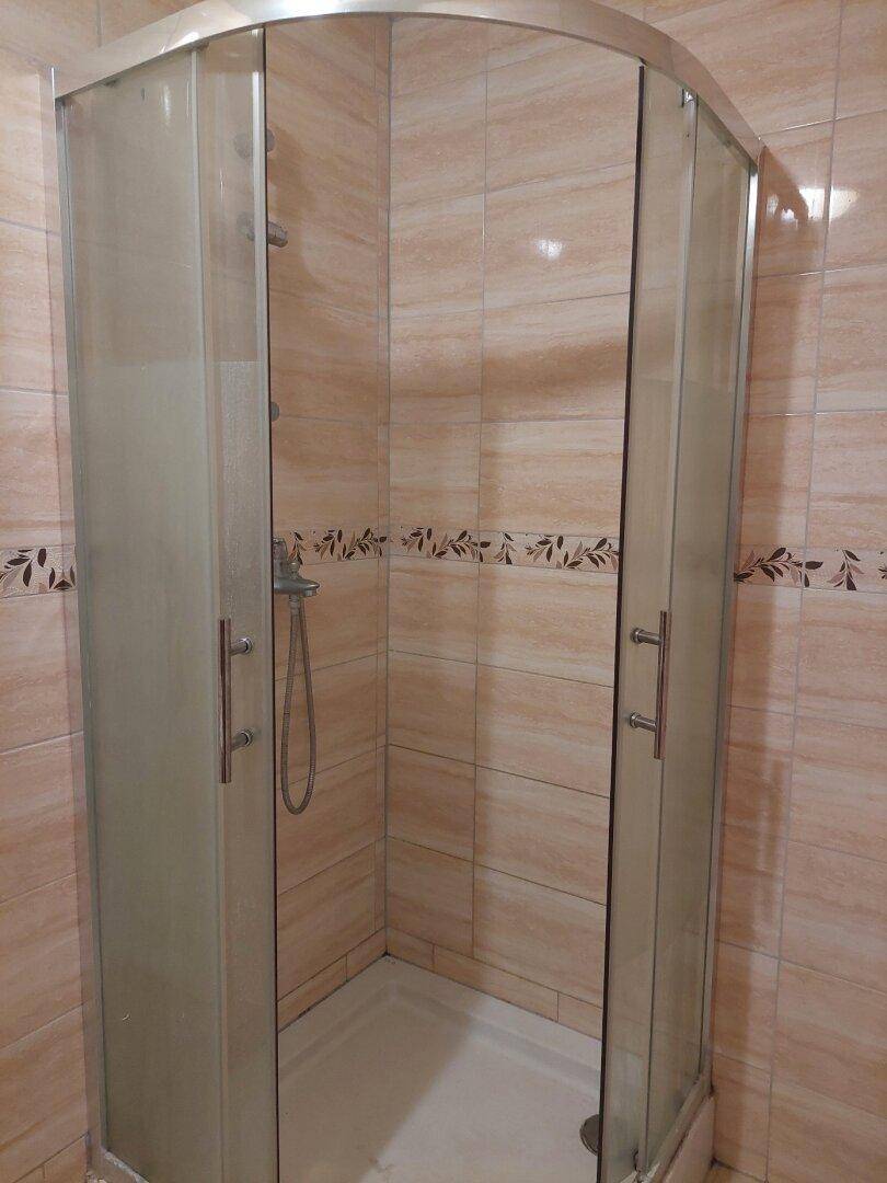 Badezimmer mit Eckduschkabine und hellen Fliesen, verziert mit einem dekorativen Band.