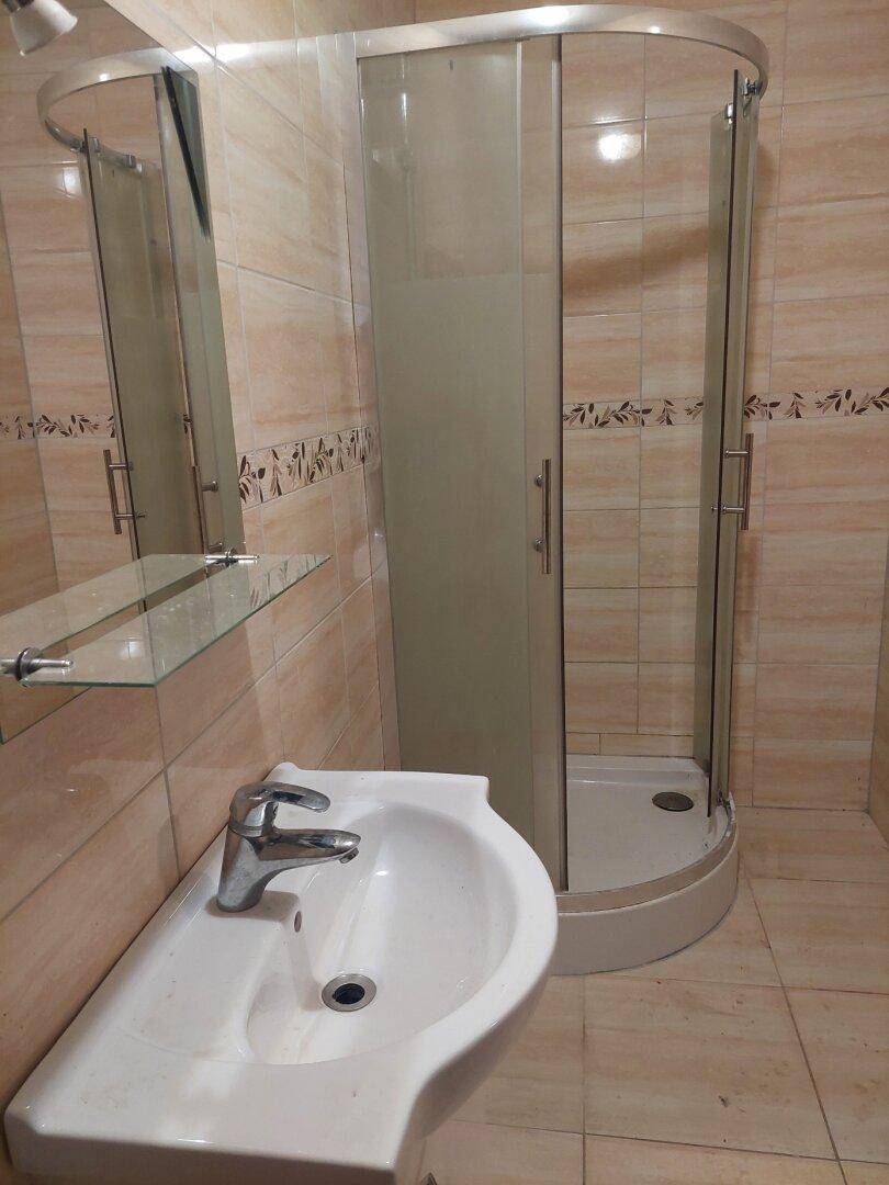 Badezimmer mit Waschbecken, Spiegel und Eckduschkabine, umgeben von hellen Fliesen.