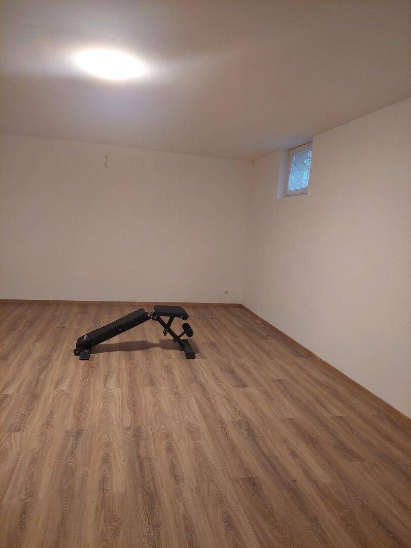 Heller Raum mit Laminatboden und einer Hantelbank, ideal für sportliche Aktivitäten.