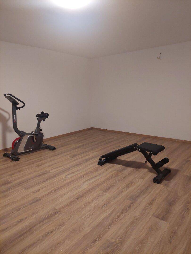 Raum mit Laminatboden, ausgestattet mit einem Heimtrainer und einer Hantelbank.