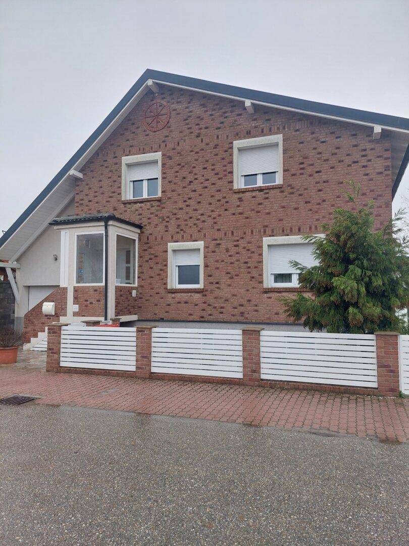 Vorderansicht des Ziegelhauses mit weißem Zaun, Erker und Rollläden an den Fenstern.