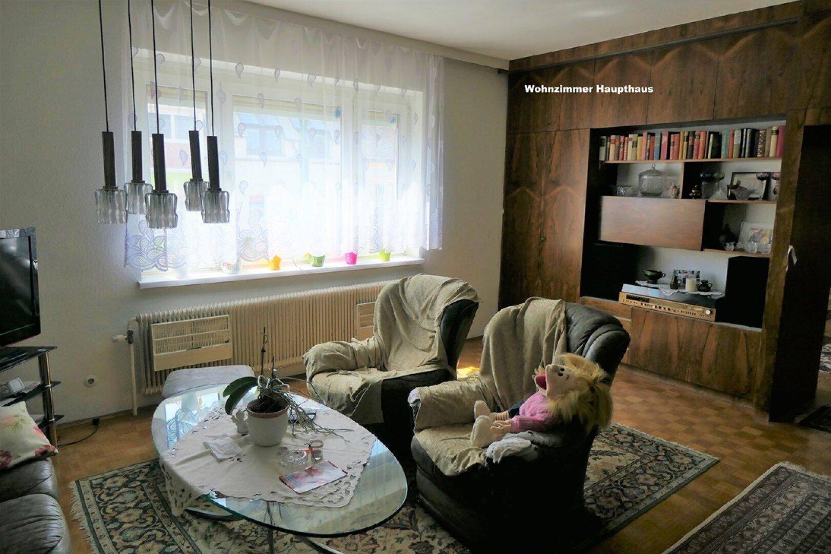 Gemütliches Wohnzimmer mit zwei Sesseln, Glastisch und einer dunklen Holzvertäfelung mit integriertem Regal.