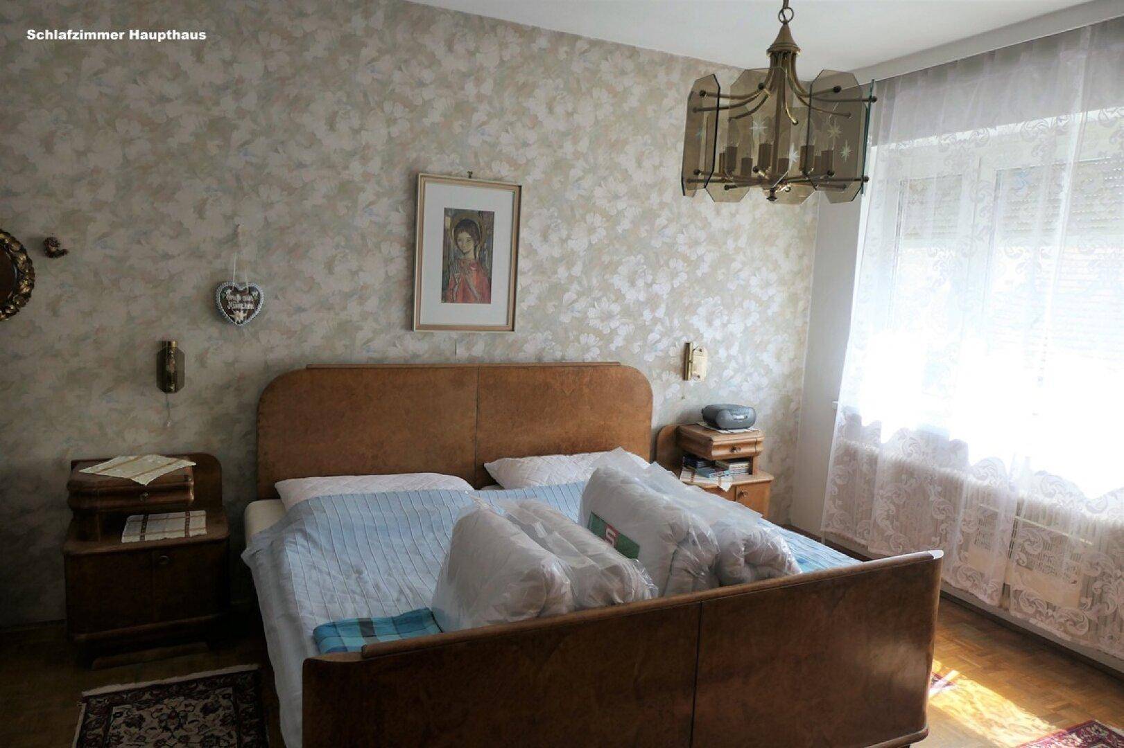 Helles Schlafzimmer mit Doppelbett, Nachttischen und gemusterter Tapete, gut beleuchtet durch ein Fenster.