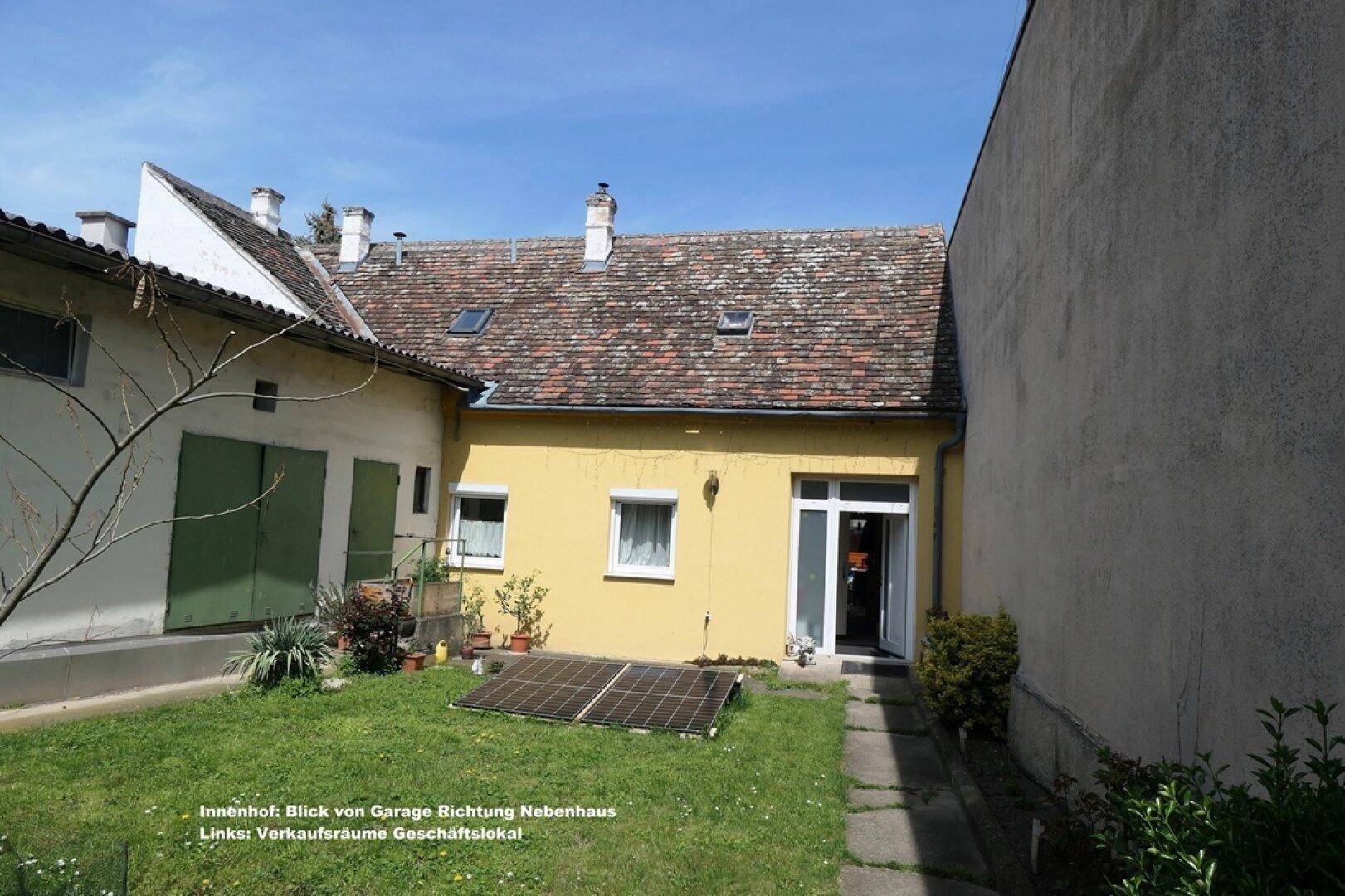 Innenhof mit Rasenfläche, gelbem Gebäude und Solarmodulen am Boden, umgeben von weiteren Bauten.