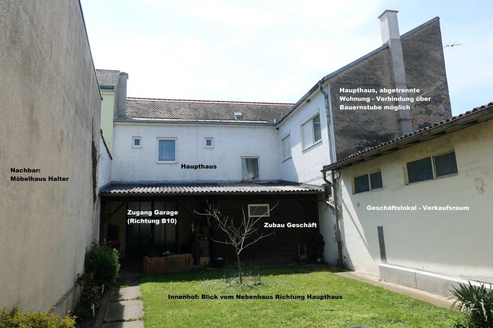 Innenhof mit Rasenfläche, Blick auf das Haupthaus und einen Anbau mit Garagenzugang.