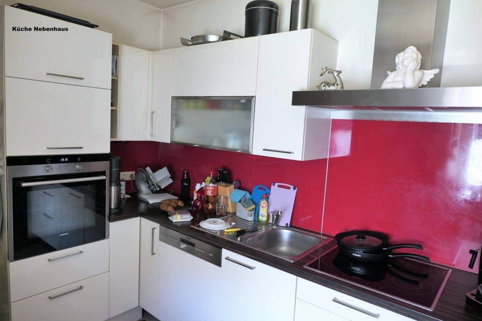Moderne Küche mit weißen Schränken, roter Rückwand und integrierten Elektrogeräten.