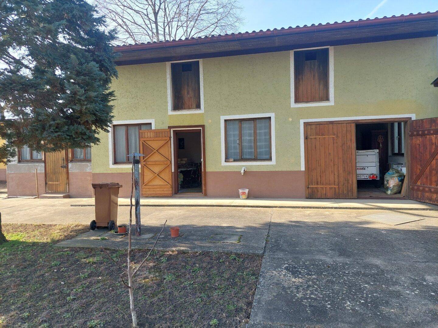 Rückseite des Hauses mit mehreren Türen und Fenstern, umgeben von Grünflächen.