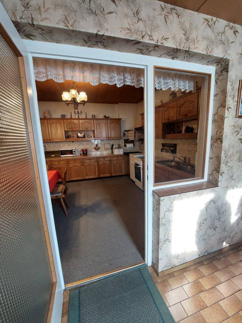 Blick in eine traditionelle Küche mit Holzschränken und Essbereich durch eine Türöffnung.