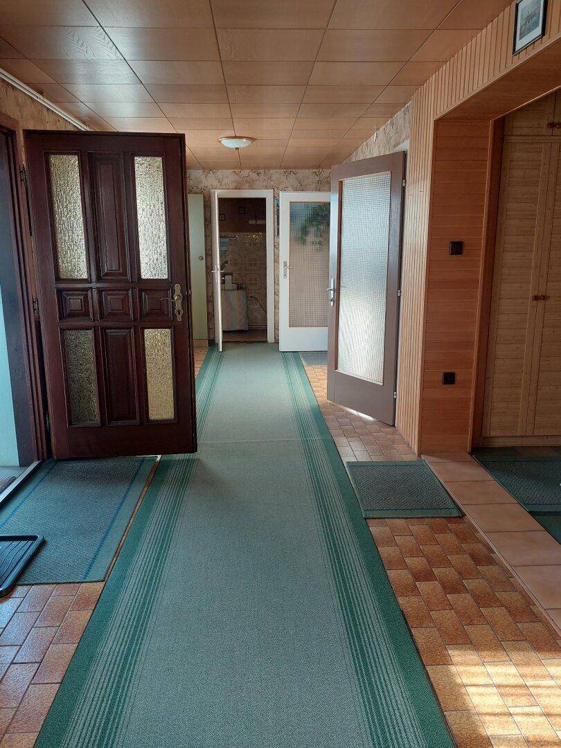 Langer Flur mit Holztäfelung an Decke und Wänden sowie gemustertem Teppichläufer.