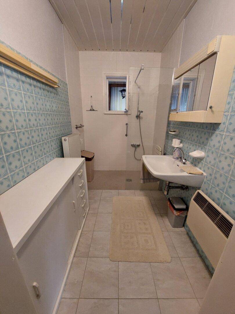 Badezimmer mit hellblauen Fliesen, Dusche und einem Waschbecken mit Spiegelschrank.