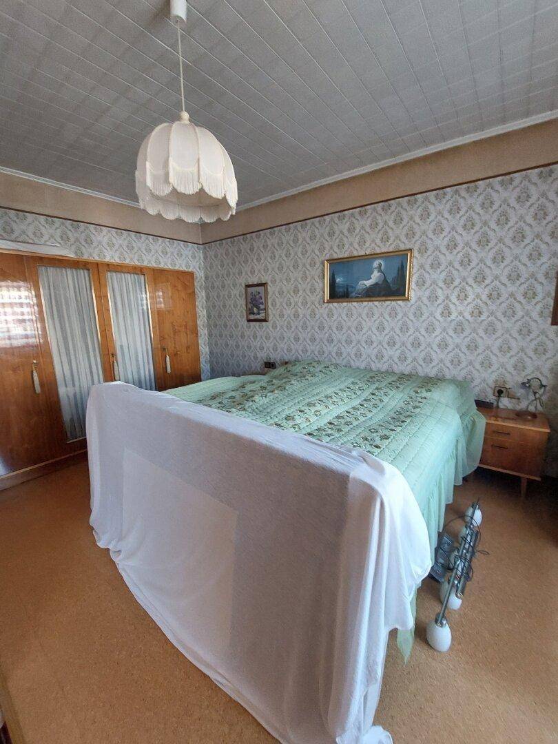 Schlafzimmer mit gemusterter Tapete, Holzschrank und einem großen Bett.