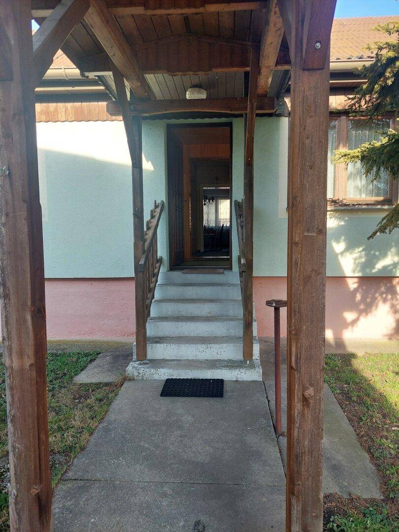 Überdachter Hauseingang mit Treppe und Holzpfosten, der ins Innere führt.