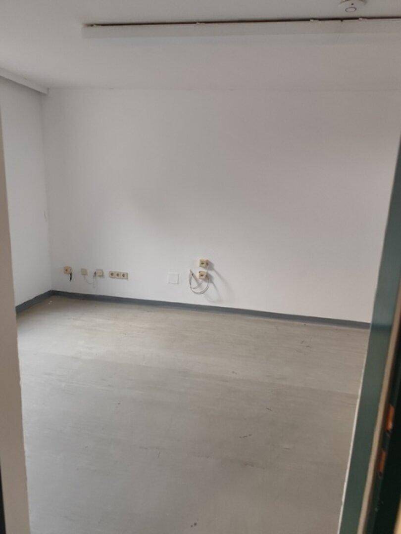 Leeres Büro mit weißen Wänden, grauem Boden und zahlreichen Steckdosen, beleuchtet von Deckenleuchten.