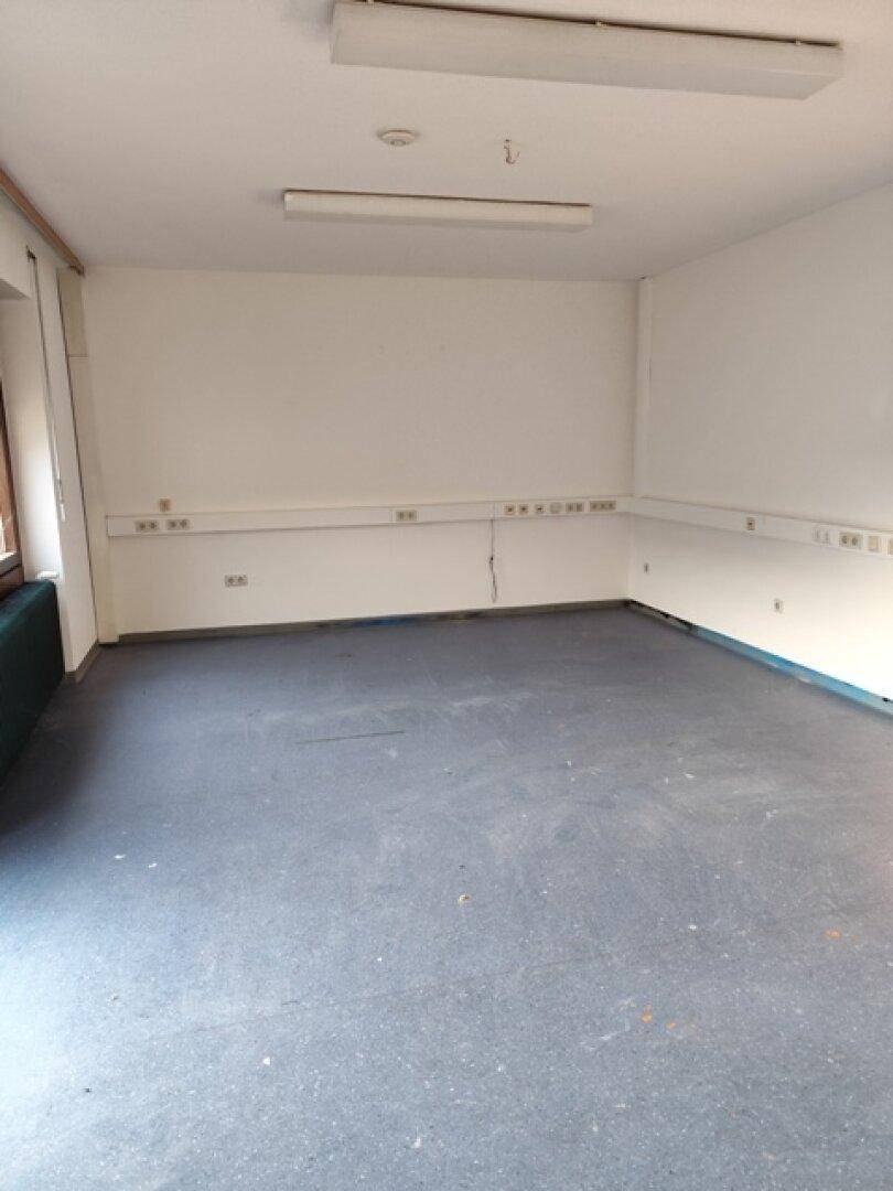 Leeres Büro mit weißen Wänden, grauem Boden und einer langen Leiste mit Steckdosen entlang der Wand.