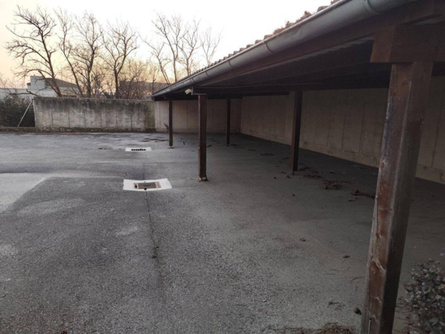 Überdachter Parkplatz mit Holzpfosten und Betonboden, bietet Schutz für Fahrzeuge.