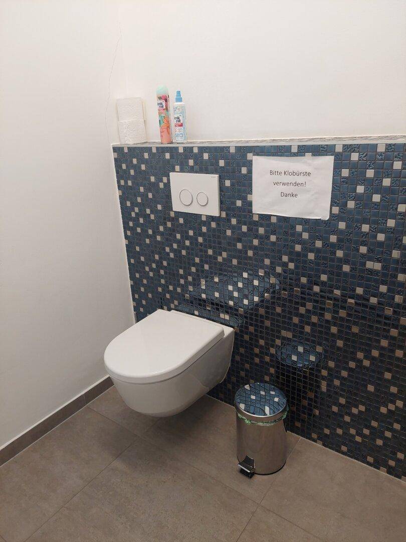 Moderne Toilette mit wandhängendem WC und dekorativen blauen Mosaikfliesen, sauber und funktional gestaltet.