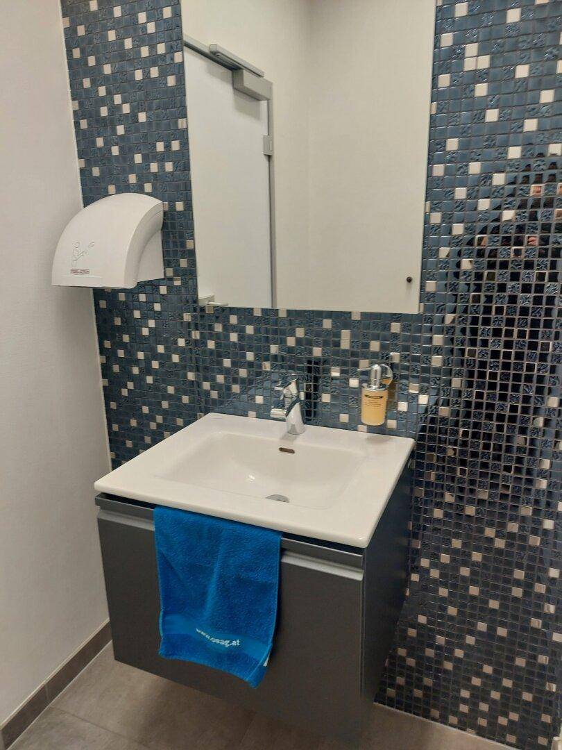 Badezimmer mit modernem Waschbecken, Spiegel und blauen Mosaikfliesen, inklusive einem Händetrockner.