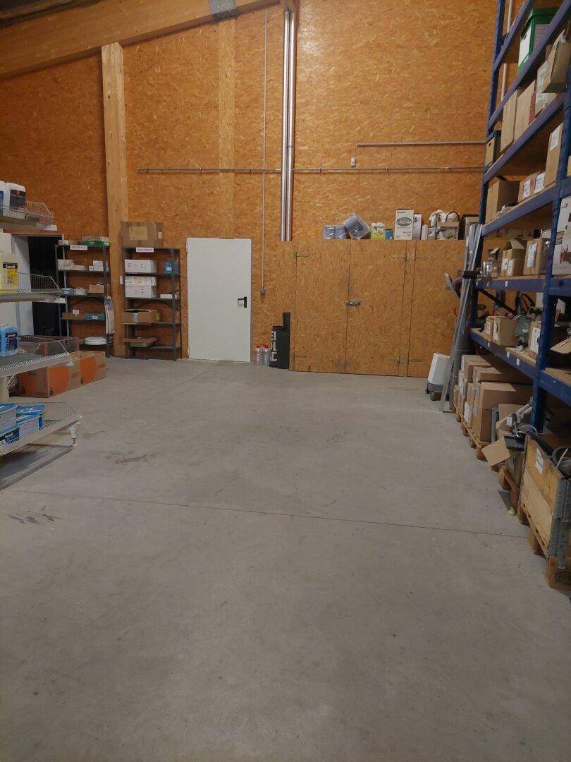 Geräumiges Lager mit hohen Regalen, Betonboden und Holzverkleidung an den Wänden, gut organisiert für Waren.