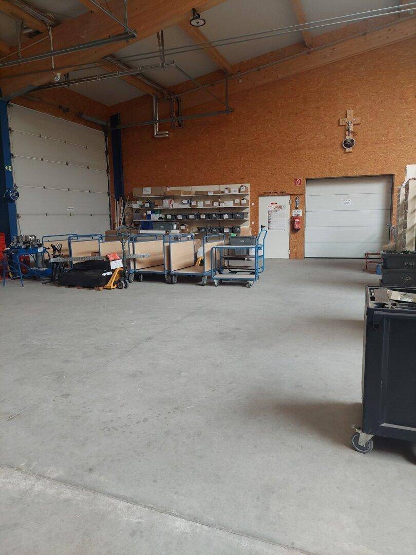 Großes Lager mit Betonboden, Rolltoren und Holzverkleidung, bietet viel Platz für Lagerung und Arbeitsgeräte.