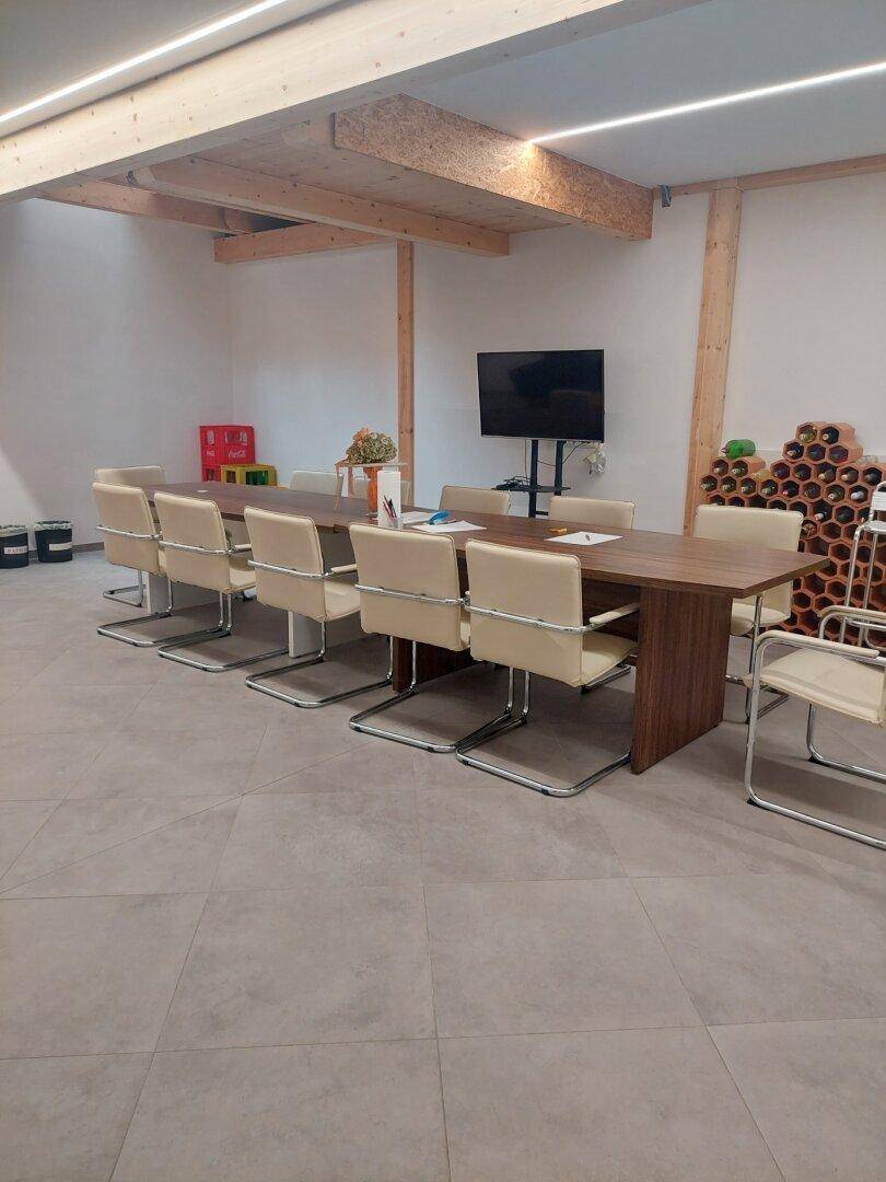 Großer Besprechungsraum mit langem Holztisch, bequemen Stühlen und Fliesenboden, unter einer Holzbalkendecke.