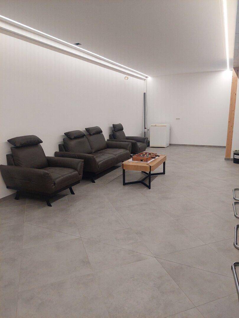 Gemütlicher Loungebereich mit dunklen Sofas, einem Couchtisch und Fliesenboden, perfekt für eine entspannte Pause.