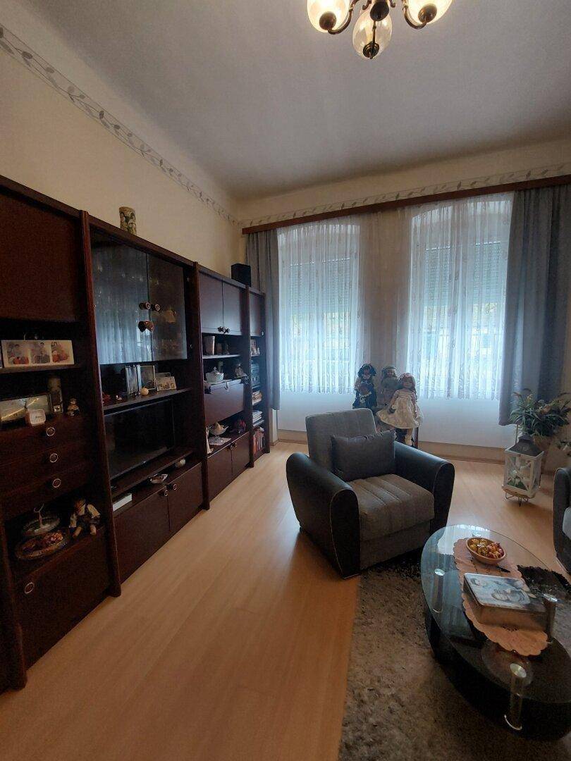 Gemütliches Wohnzimmer mit Holzfußboden, dunklen Möbeln und großen Fenstern mit Vorhängen.