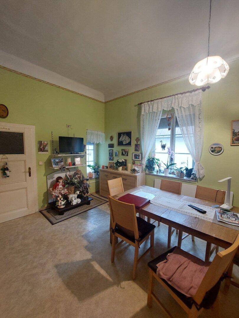 Esszimmer mit Holztisch und Stühlen, grünen Wänden und einem Fenster mit Vorhängen.