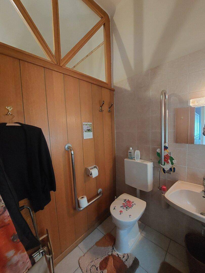 Gäste-WC mit Holzvertäfelung, Waschbecken und Haltegriffen für zusätzliche Sicherheit.