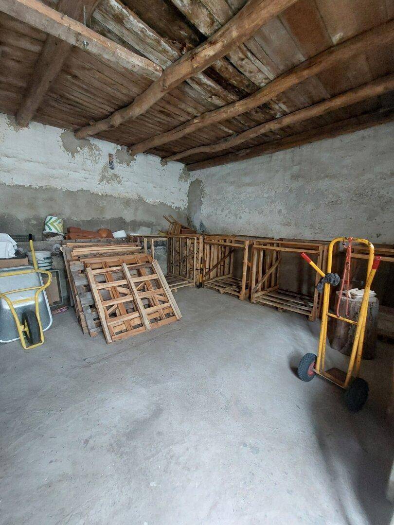Rustikaler Abstellraum mit sichtbaren Holzbalken, Betonboden und gestapeltem Holz.
