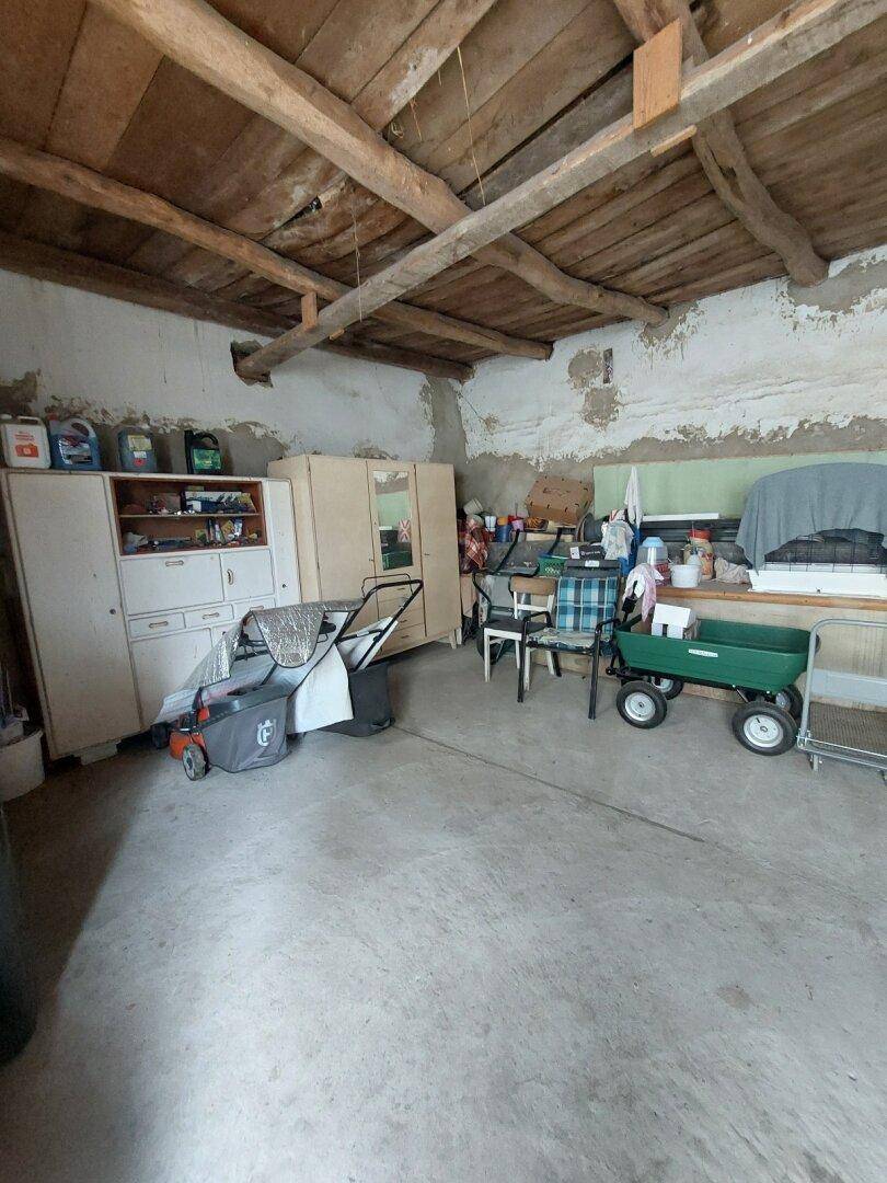 Geräumiger Abstellraum mit Betonboden, Holzbalken und verschiedenen Gartengeräten.