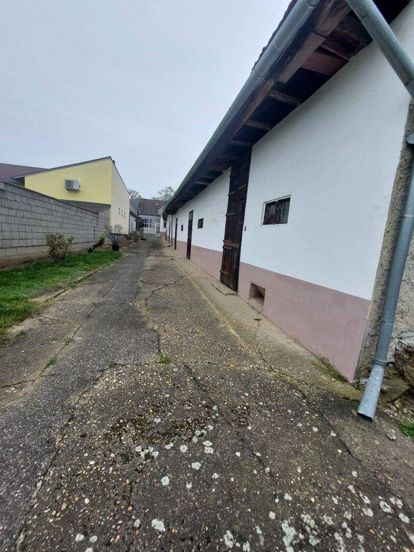 Langer Gebäudekomplex mit Betonweg und einfachen Holztüren, umgeben von Grünflächen.