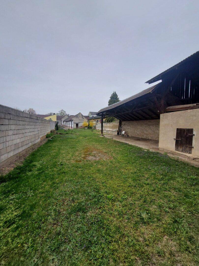 Weitläufiger Gartenbereich mit Rasen und einem großen Holzschuppen, umgeben von einer Mauer.