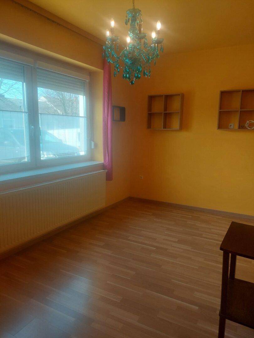 Helles Zimmer mit gelben Wänden, Holzfußboden und einem auffälligen blauen Kronleuchter.