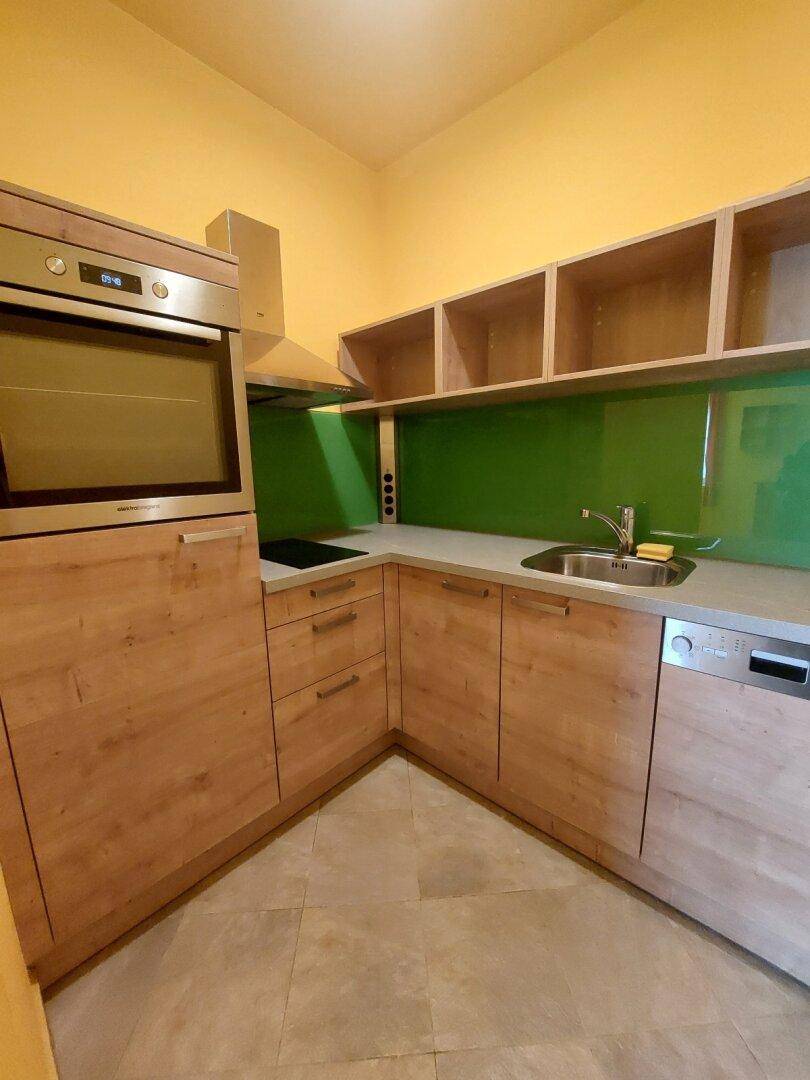 Kleine Küchenzeile mit Holzschränken, grünem Fliesenspiegel und integrierten Geräten.