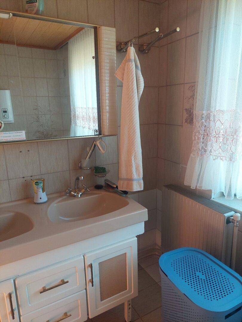 Badezimmer mit Doppelwaschbecken, Spiegelschrank und Heizkörper unter dem Fenster.