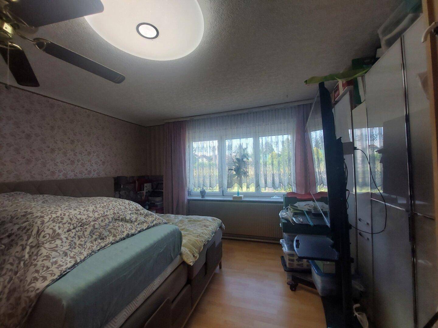 Schlafzimmer mit Doppelbett, gemusterter Tapete, Deckenventilator und großem Fenster.