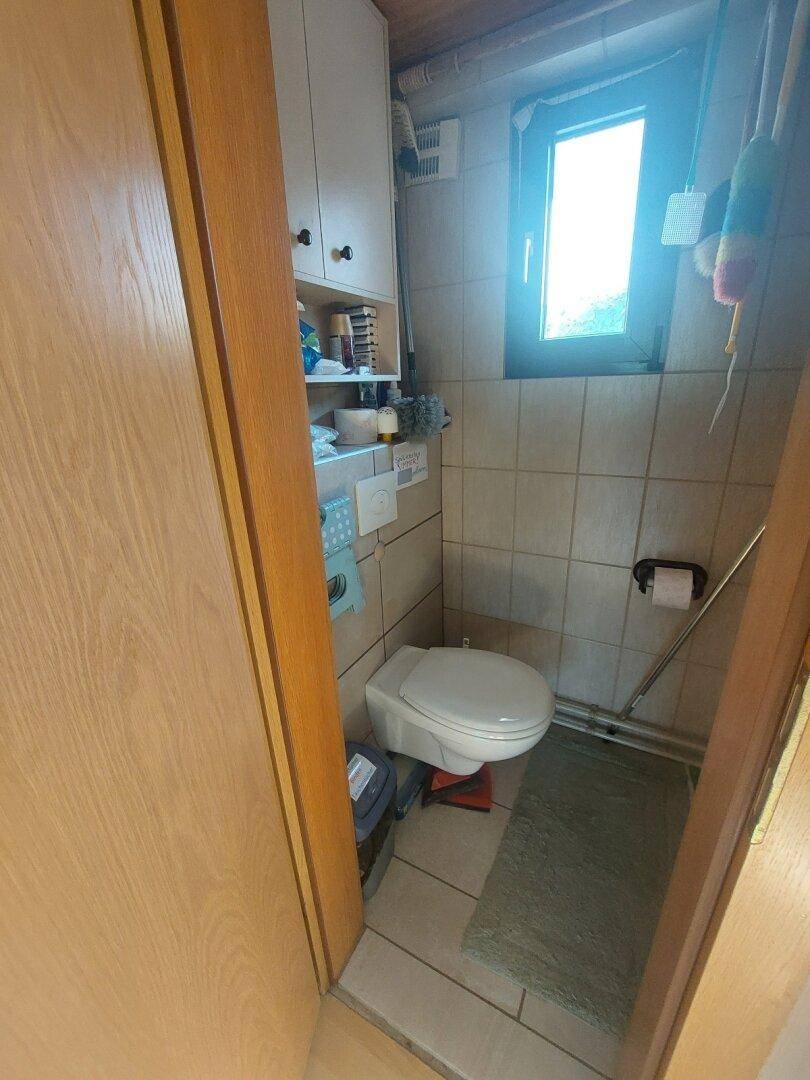 Kleines Gäste-WC mit Wand-WC, hellen Fliesen und einem Fenster für Belüftung.