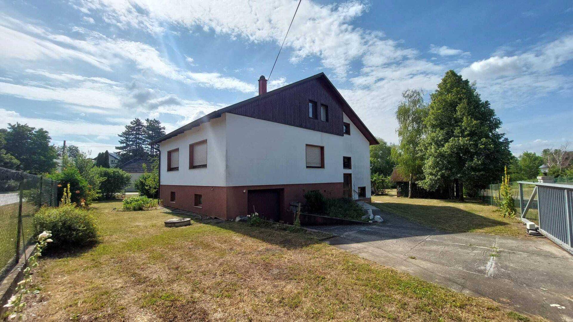 Ansicht des Hauses von der Seite mit Zufahrt und Gartenbereich unter blauem Himmel.