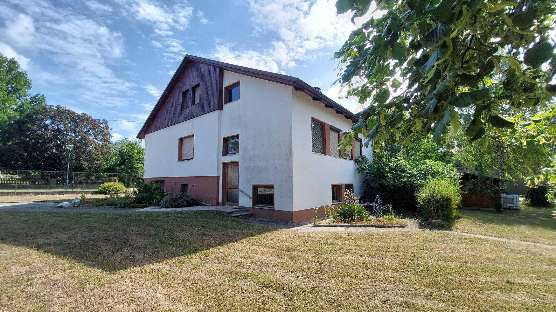 Das Wohnhaus mit weißer Fassade und braunem Dach, umgeben von einem grünen Garten.