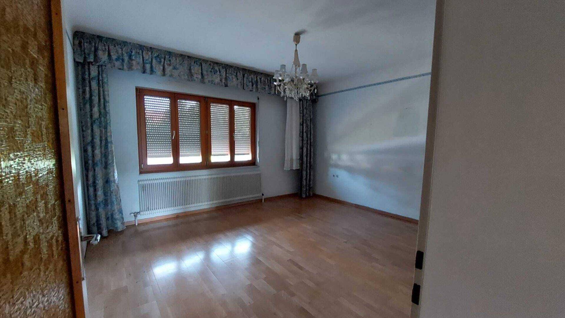 Leeres Zimmer mit Holzboden und großen Fenstern, bereit zur individuellen Gestaltung.
