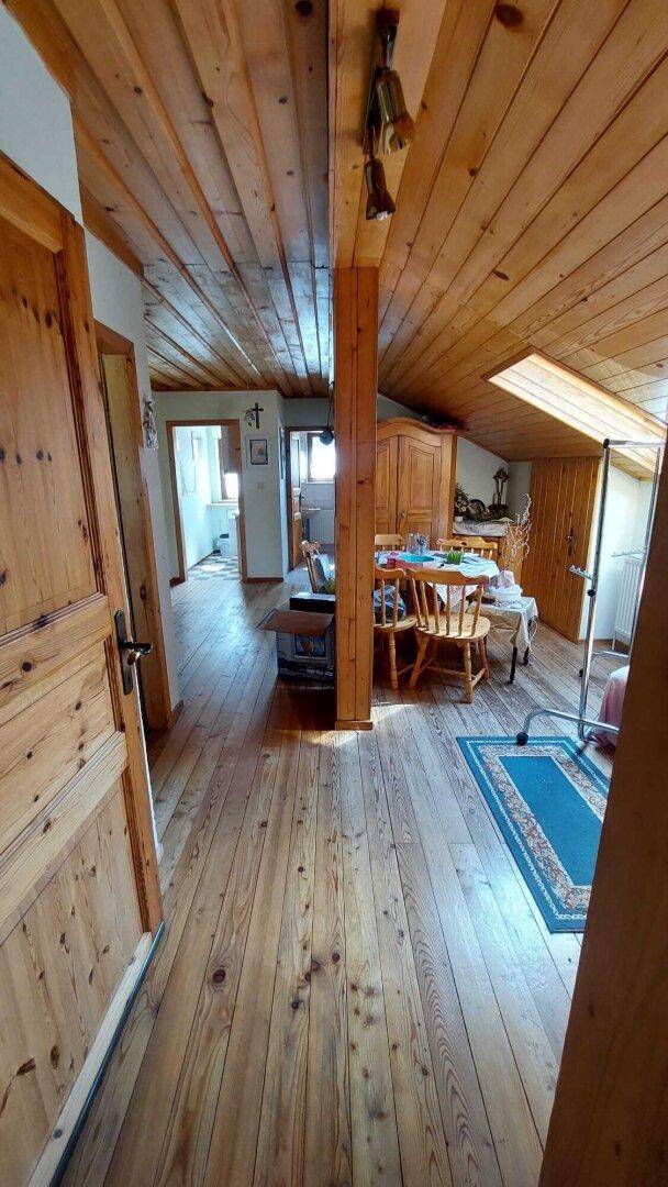 Dachgeschosszimmer mit schräger Holzdecke, Holzboden und einem Esstisch.