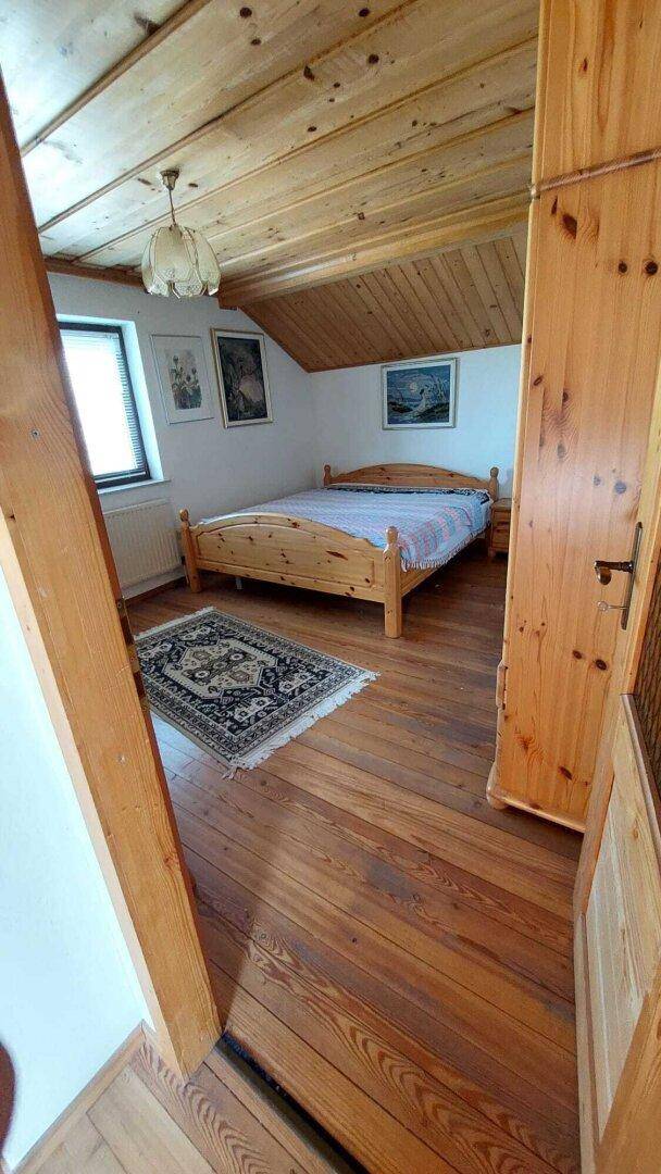 Schlafzimmer im Dachgeschoss mit Holzboden, schräger Holzdecke und einem Doppelbett.