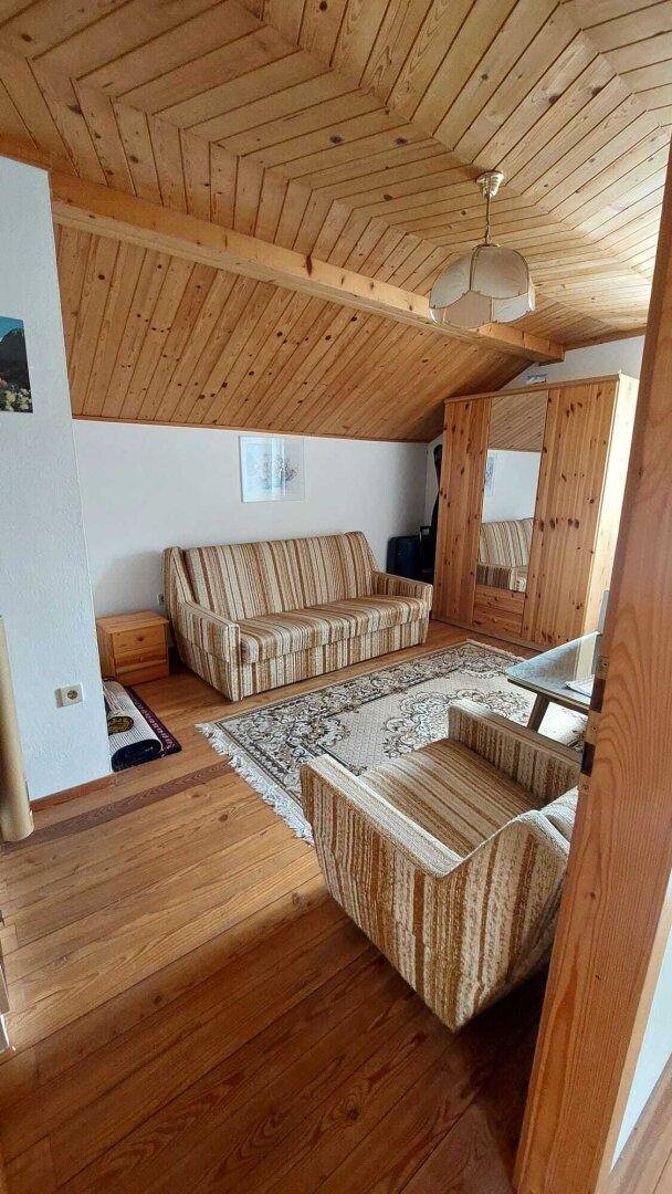 Gemütliches Wohnzimmer im Dachgeschoss mit Holzboden, schräger Holzdecke und Sofa.