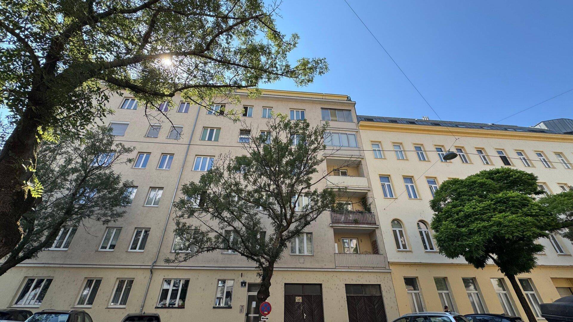 Fassade eines Mehrfamilienhauses mit vielen Fenstern und Bäumen davor.