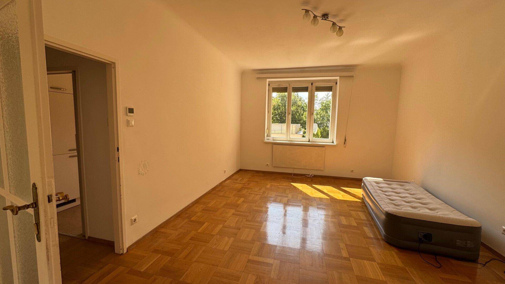 Helles Wohnzimmer mit Parkettboden und großem Fenster, das viel Tageslicht hereinlässt.