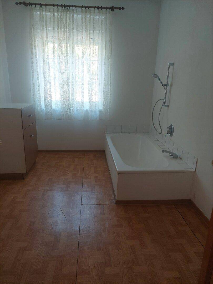 Badezimmer mit Badewanne, Fenster und Holzparkettboden.