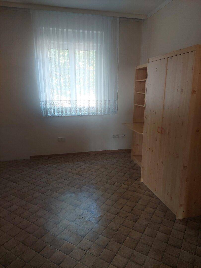 Helles Schlafzimmer mit Teppichboden, Holzschrank und großem Fenster.