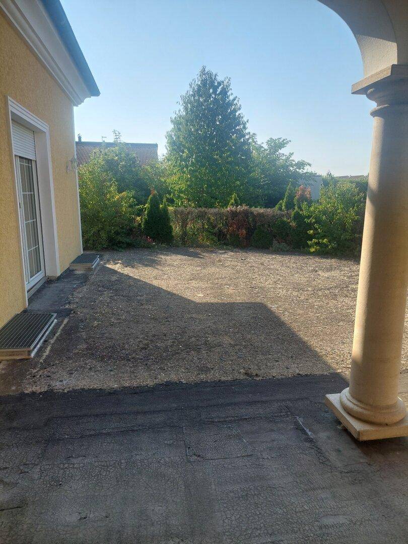 Große, unmöblierte Terrasse mit Säulen und Blick auf den Garten.