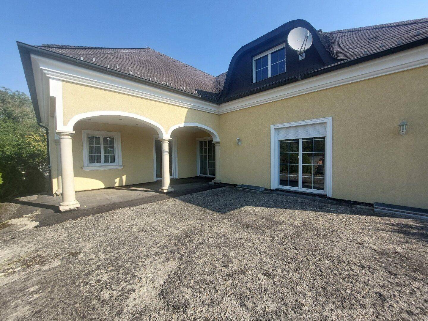 Rückansicht der Villa mit großer Terrasse, Säulen und Mansarddach.