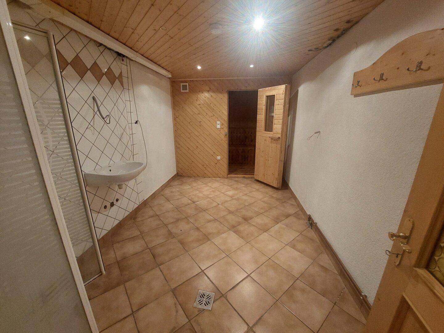 Vielseitiger Raum mit Holzdecke, Fliesenboden, Waschbecken und einer integrierten Sauna für Entspannung.